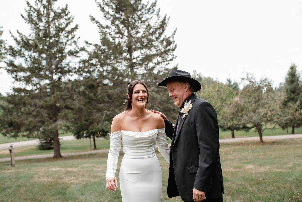 A couple in wedding attire stands together outdoors with pine trees in the background on their special day.
