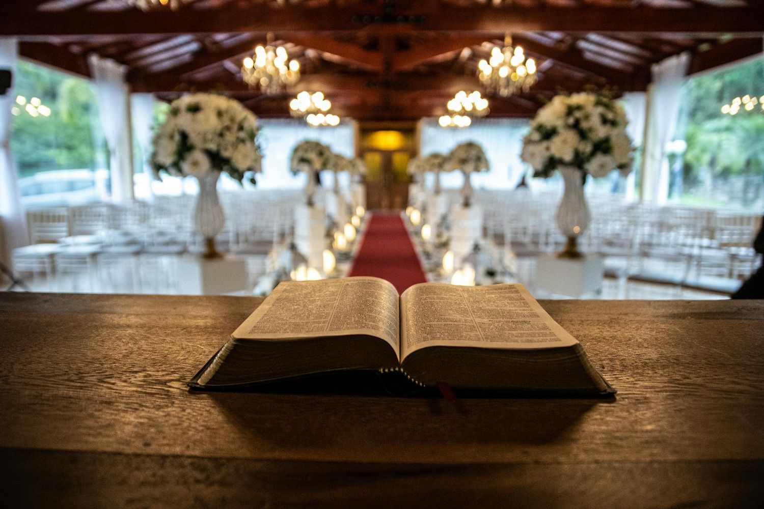 An open Bible on wooden podium with elegant wedding ceremony venue and floral arrangements in background.