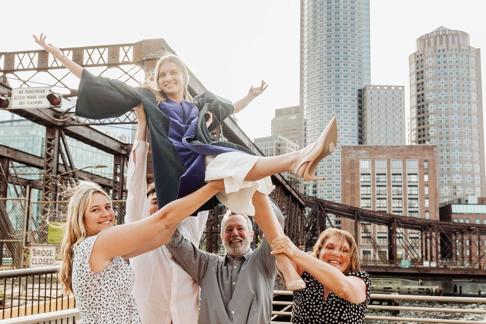 A group of friends strike a playful pose on a city bridge with urban skyscrapers in the background.