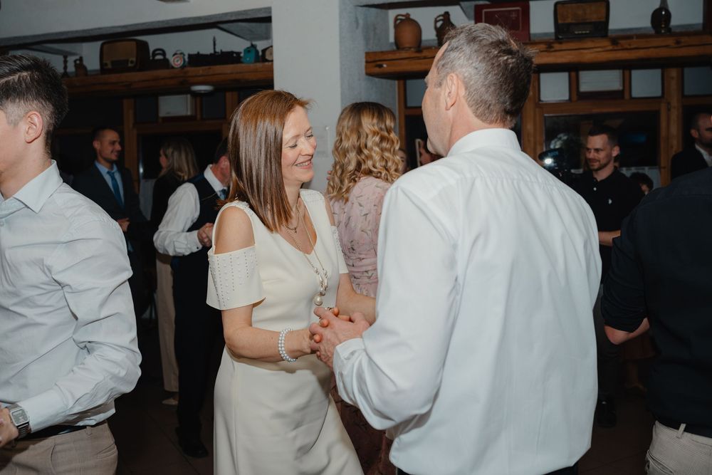 Wedding guests dancing together at an indoor reception with exposed beams and rustic shelving in the background.