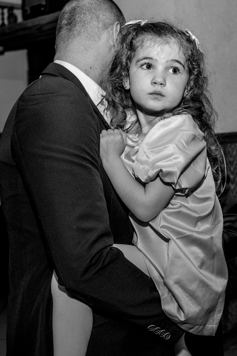 Black and white photo of a young girl in a satin dress being held while dancing at a formal event.