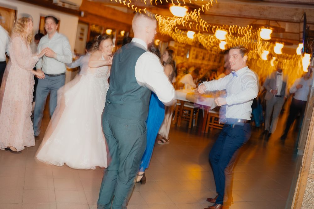 Wedding reception guests dancing on a glowing dance floor beneath ornate chandeliers in an elegant indoor venue.