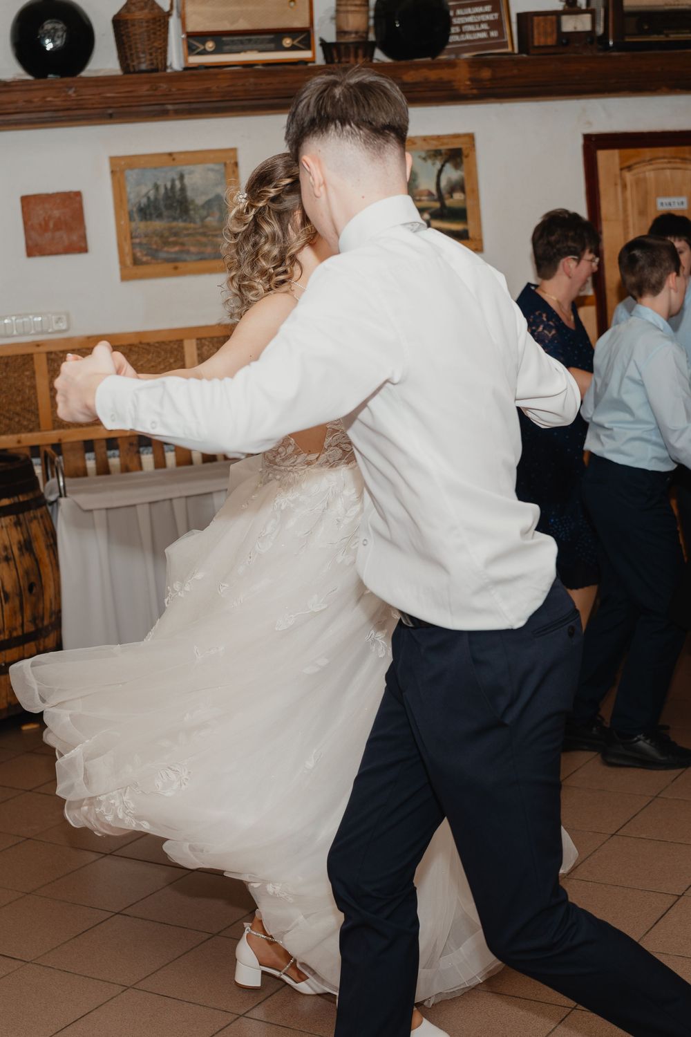 A couple dances at their wedding reception, with the bride in a flowing white dress and groom in dress shirt and slacks.