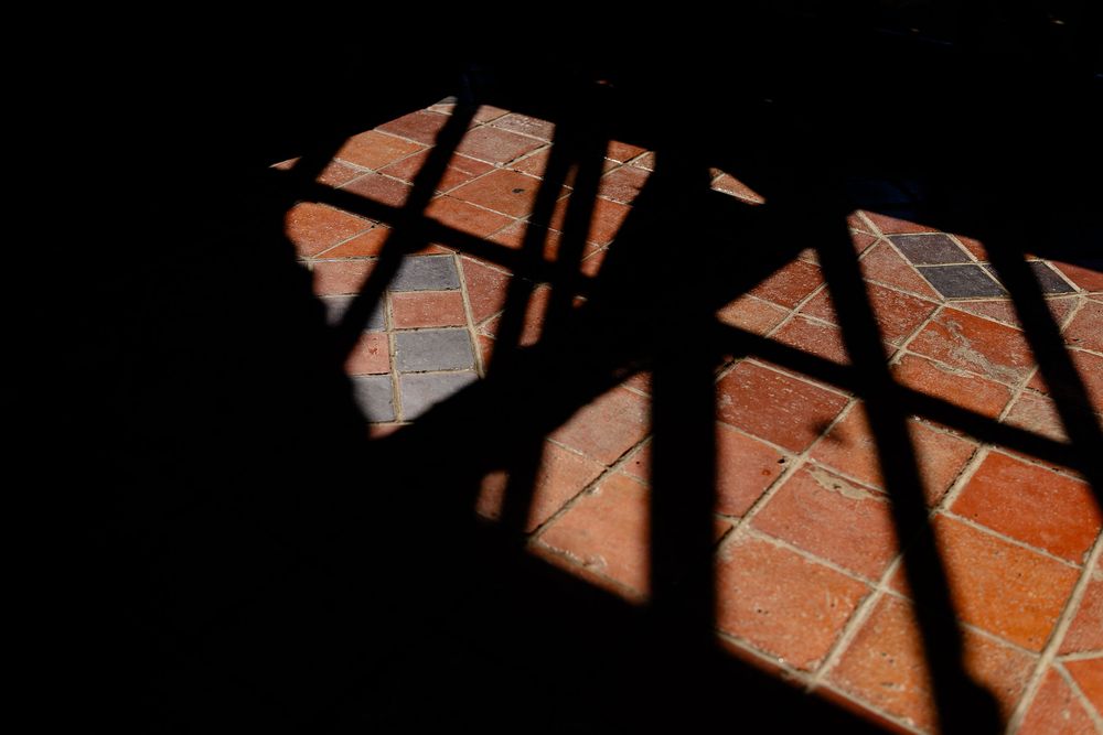 Dramatic shadows cast geometric patterns across terracotta floor tiles in sunlight.