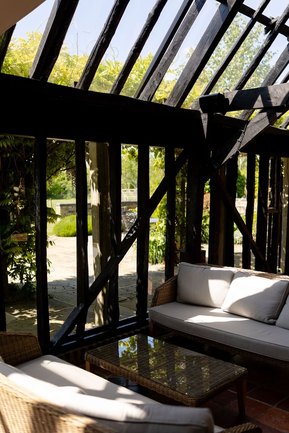 Sunlit garden room with wooden beams features a comfortable white cushioned seating area and glass coffee table.
