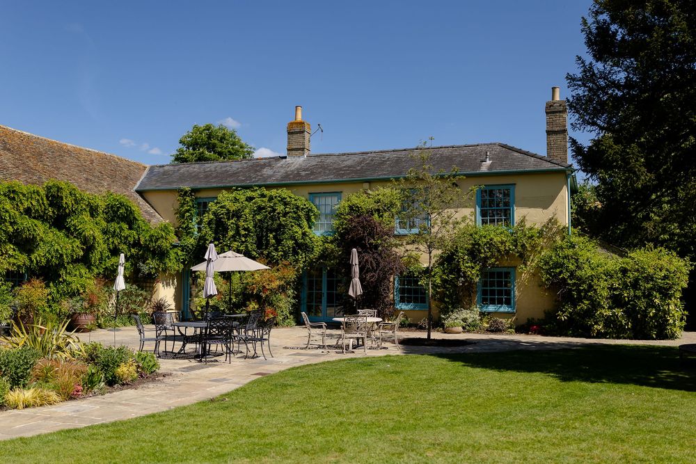 A charming yellow country house with a landscaped garden patio and outdoor dining furniture on a sunny day.