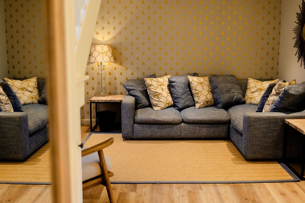 Cozy living room interior with gray sofas, decorative pillows, and polka dot wallpaper lit by ambient lamp lighting.