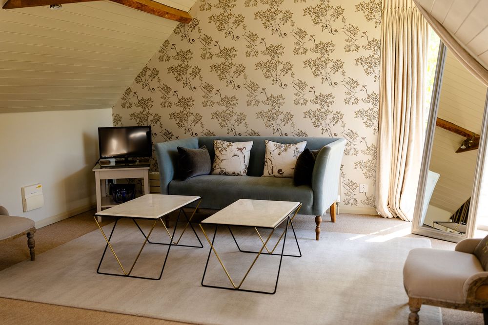 Cozy attic living room with gray sofa, modern coffee tables, and floral wallpaper accent wall in neutral tones.