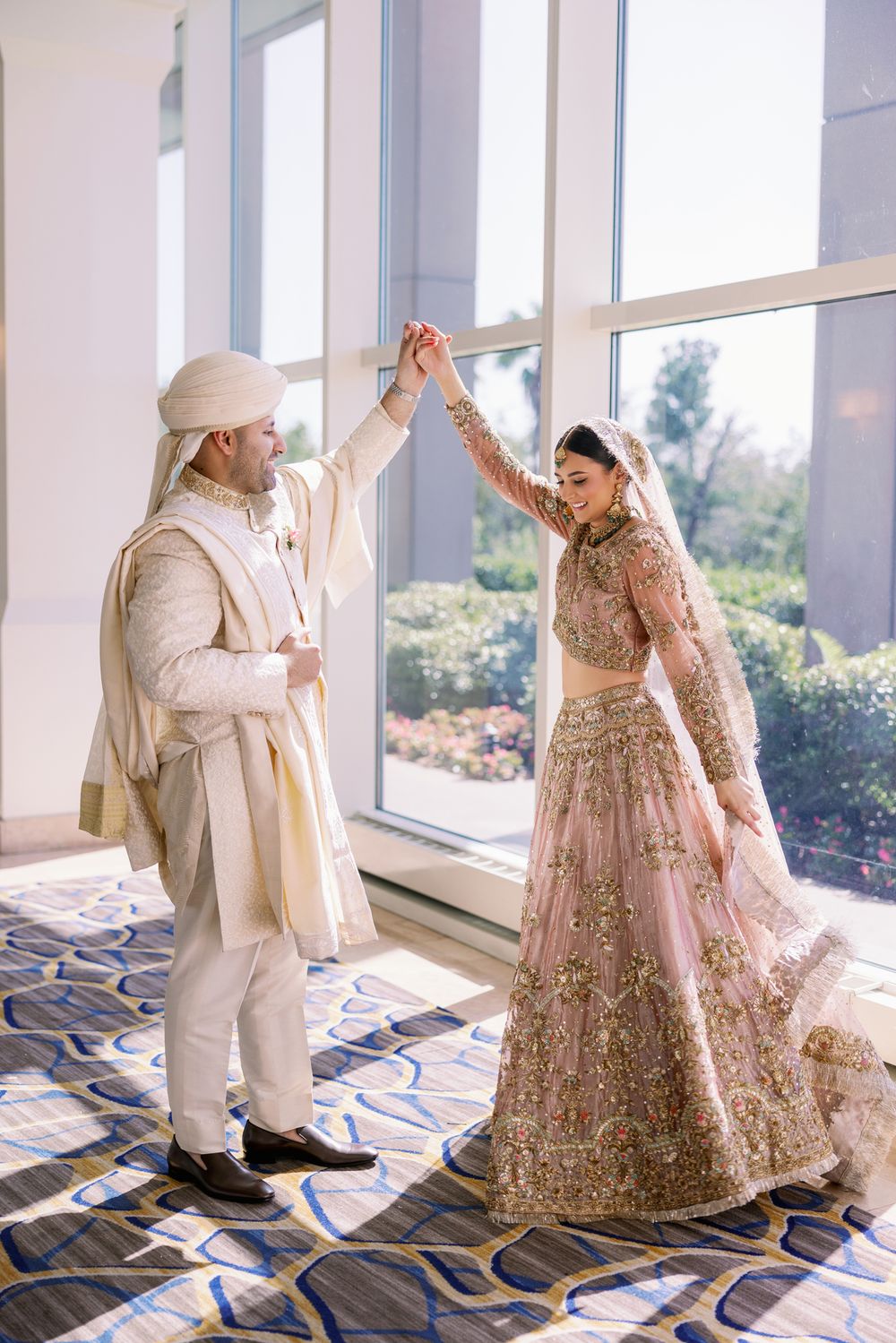 Joyful dancing moment between couple in cream and pink traditional South Asian wedding attire.