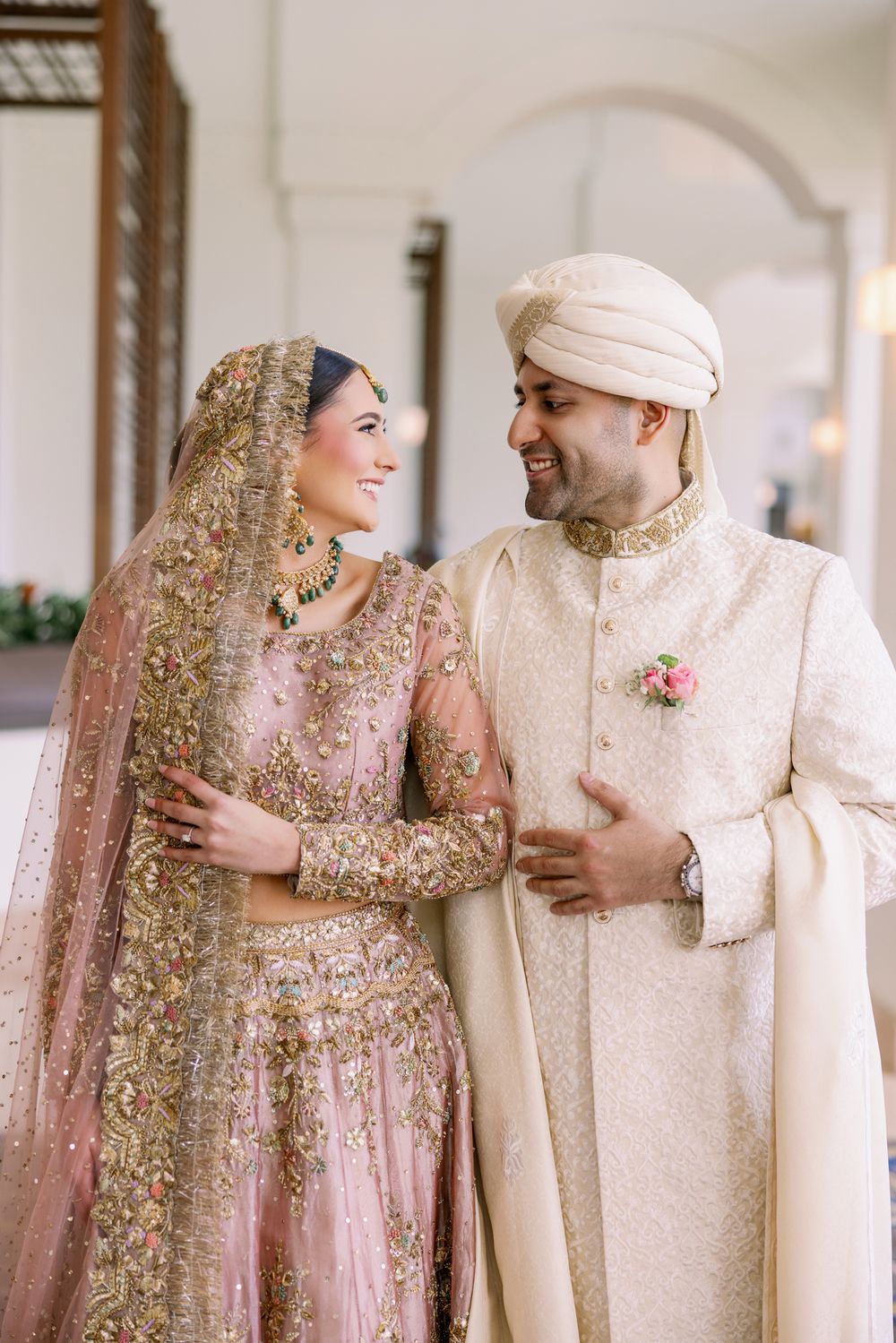 A couple in traditional wedding attire shares a joyful moment in an elegant hallway.