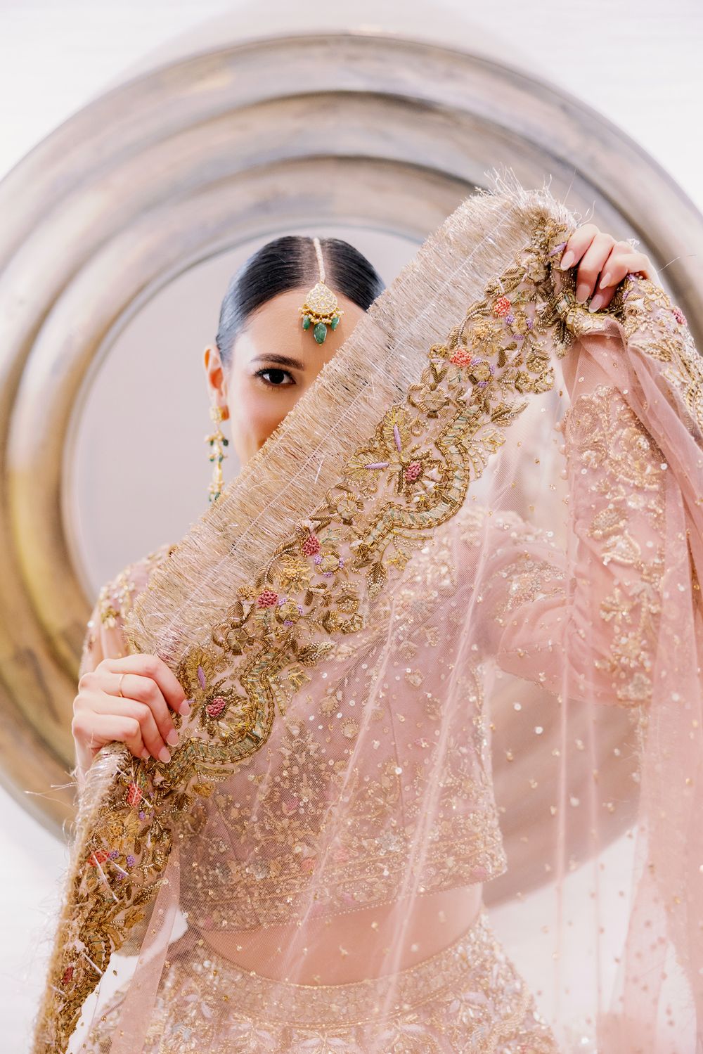 Bride in pink embroidered wedding lehenga poses behind her veil.