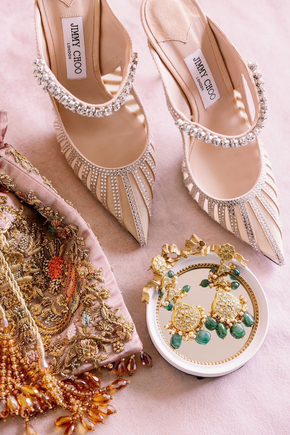 Elegant bridal shoes and jewelry featuring crystals and pearls arranged on pink fabric.
