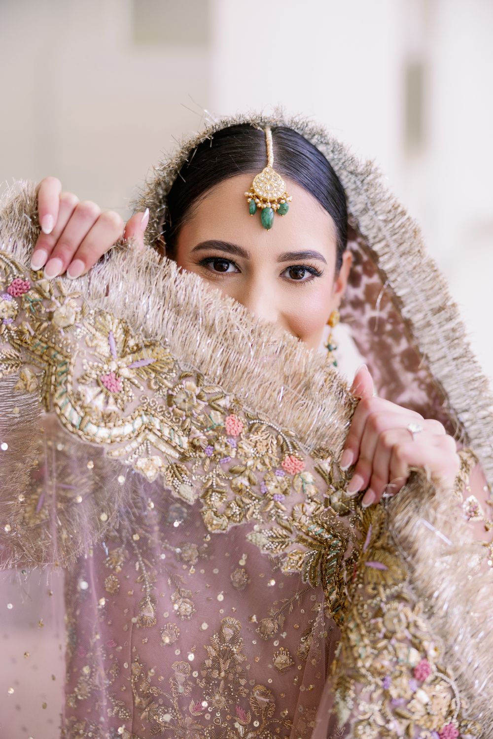 A bride in traditional attire playfully peeks through her embroidered veil.