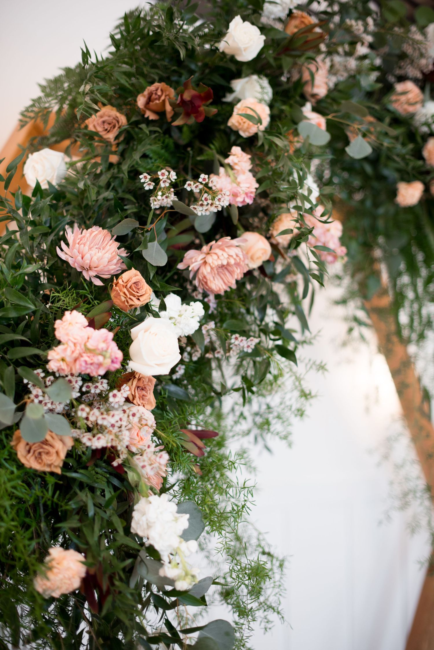 Romantic floral arch decorated with peach roses, white flowers, and cascading greenery against a white backdrop.