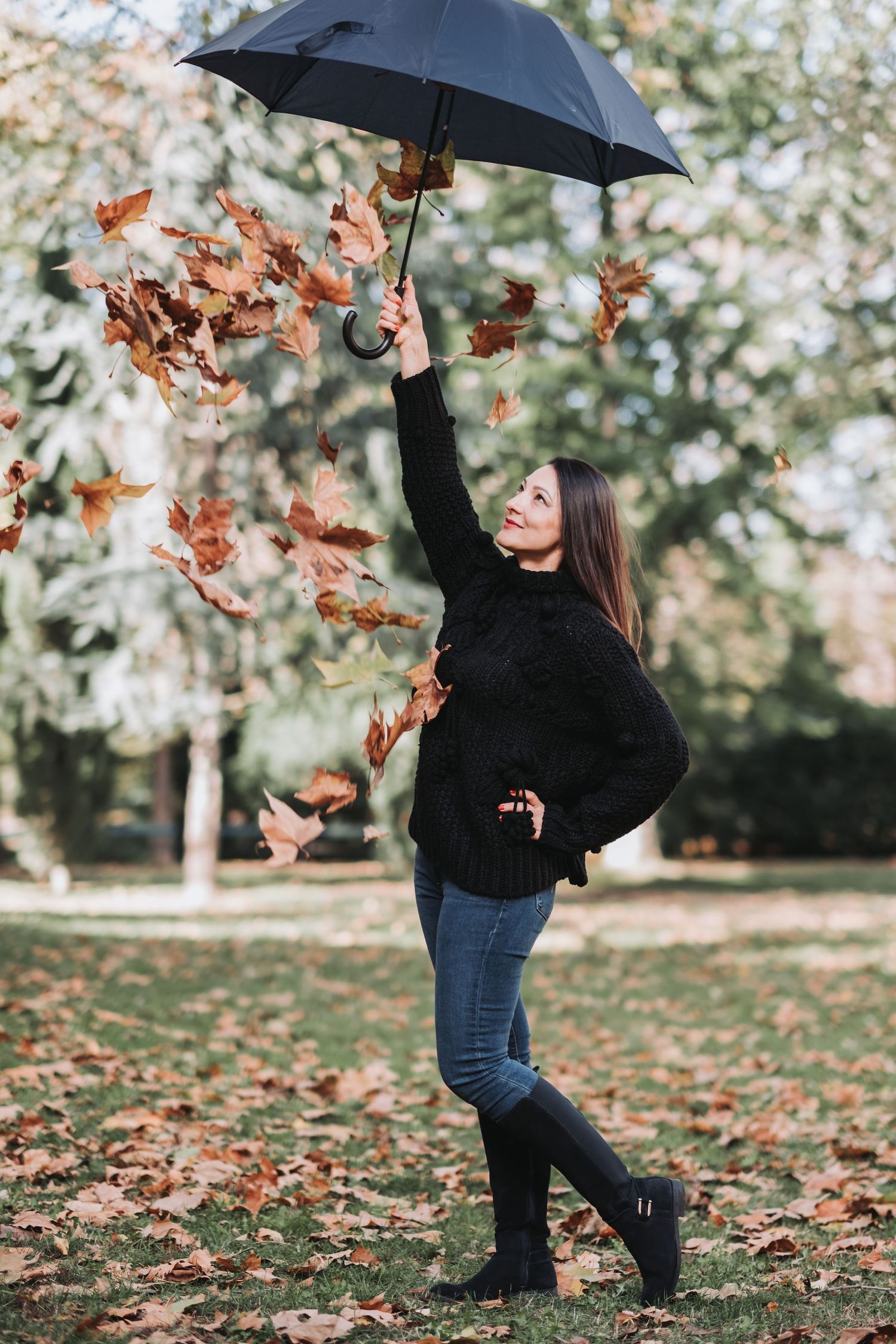 Playful autumn portrait of woman with umbrella surrounded by falling leaves.