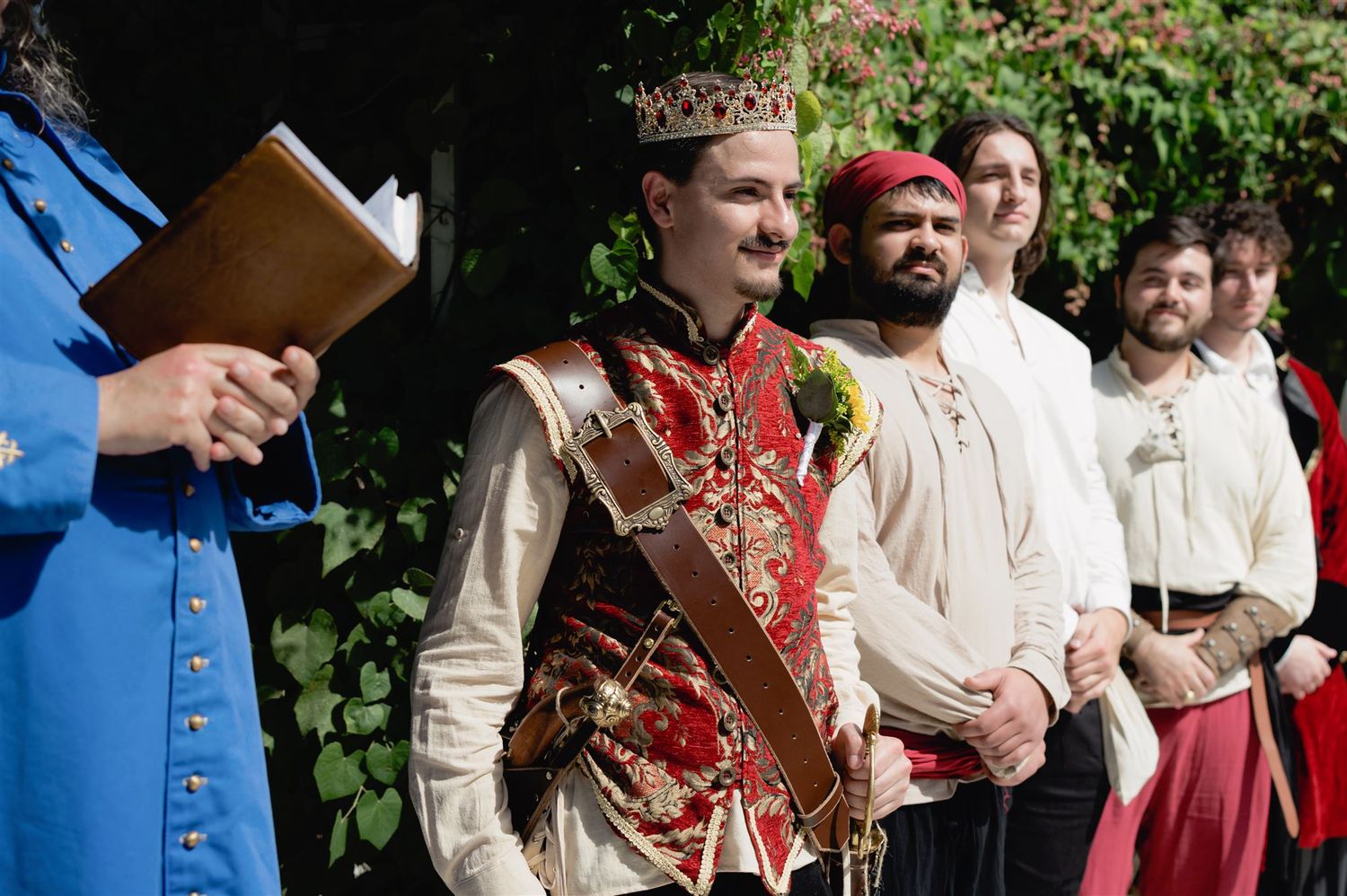 Period performers in medieval Renaissance costumes gather outdoors during a historical reenactment event.