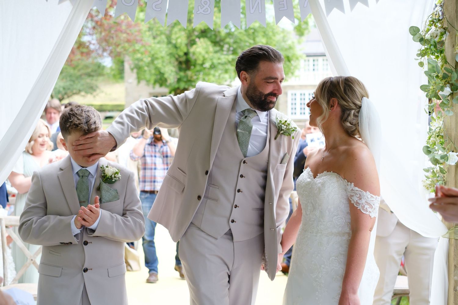 Groom getting ready to kiss his bride. His best man is his son. Groom is trying to cover son's eyes.