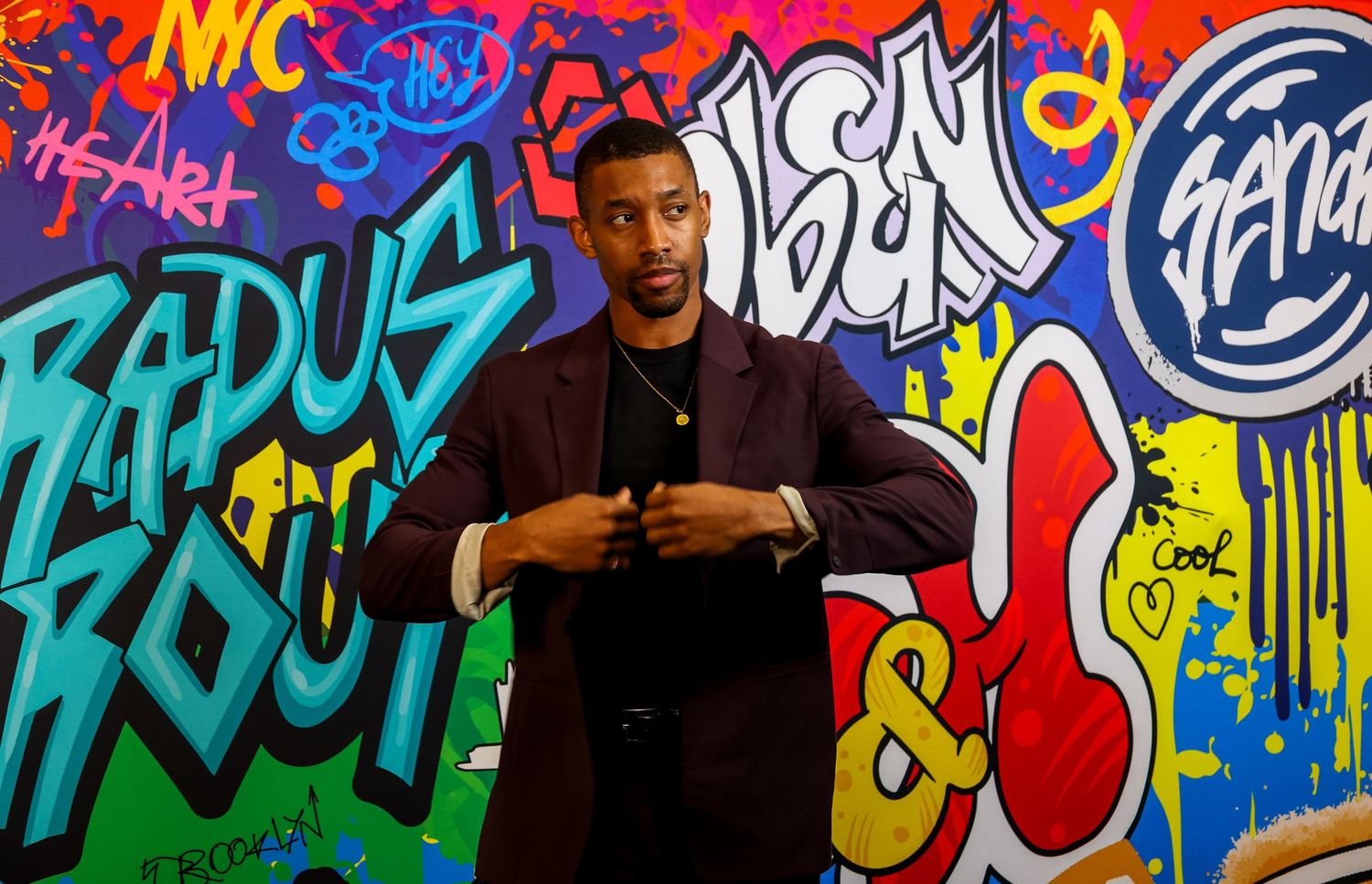 Someone stands in front of a vibrant graffiti wall with colorful street art featuring letters and designs in blue and red tones.