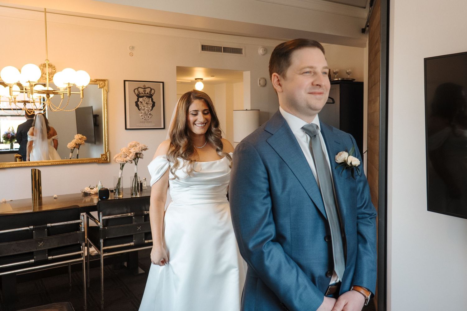 A bride and groom share a romantic moment in a brightly lit hallway with elegant wall sconces and decor.