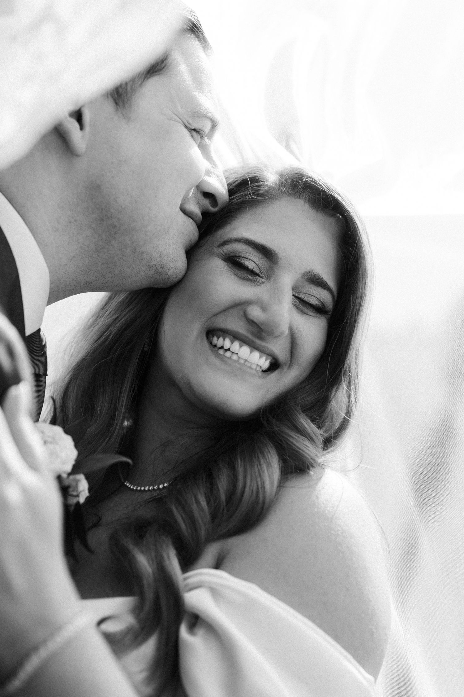 Black and white romantic wedding photo showing tender moment and genuine laughter between joyful newlyweds.