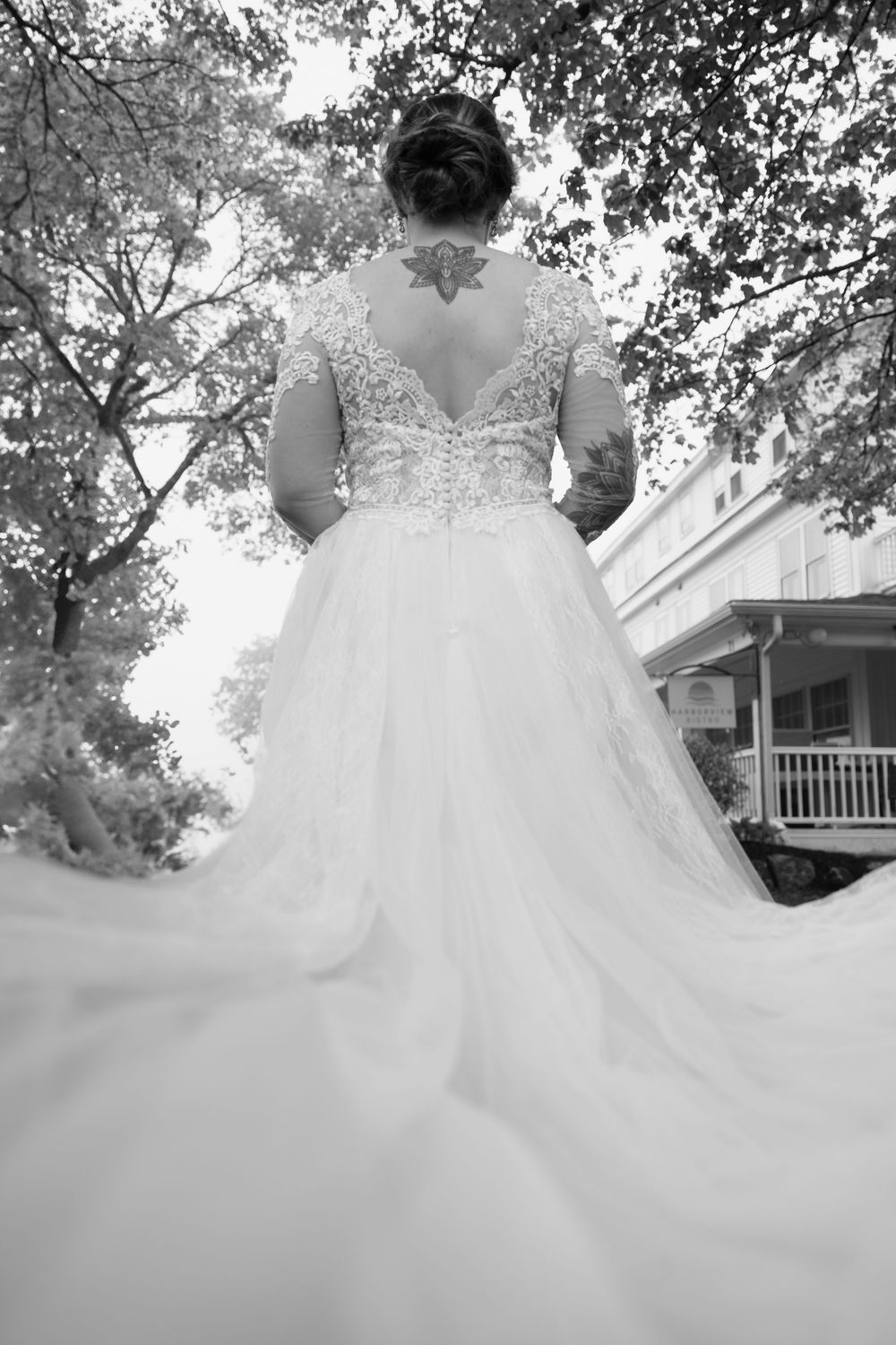 Back view of an elegant wedding dress with intricate lace details and flowing tulle skirt against a garden backdrop.