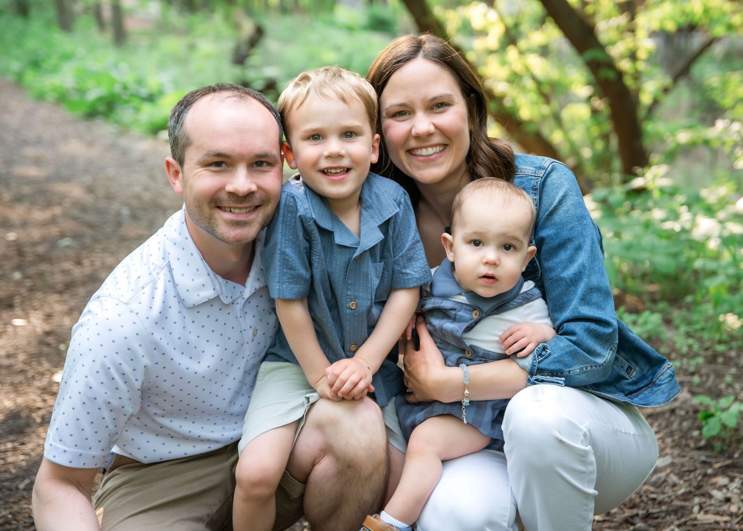 Family portrait session in a lush green forest setting with casual coordinated outfits in white and denim.