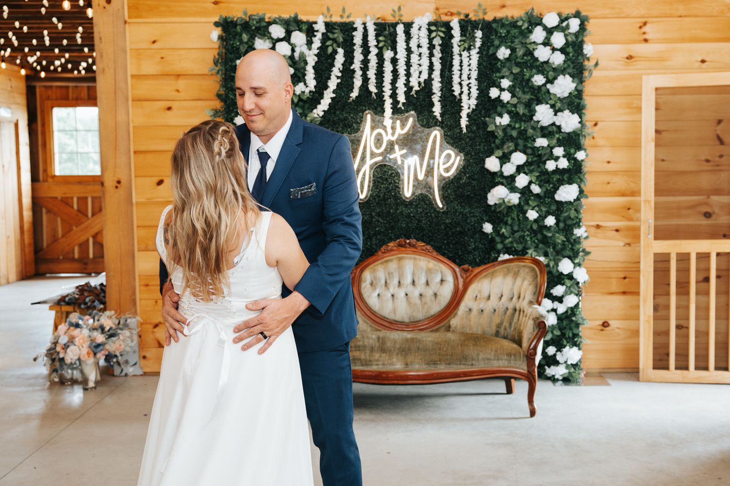 A couple embraces during their wedding ceremony in a rustic wooden barn venue decorated with elegant white floral arrangements. First dance.
