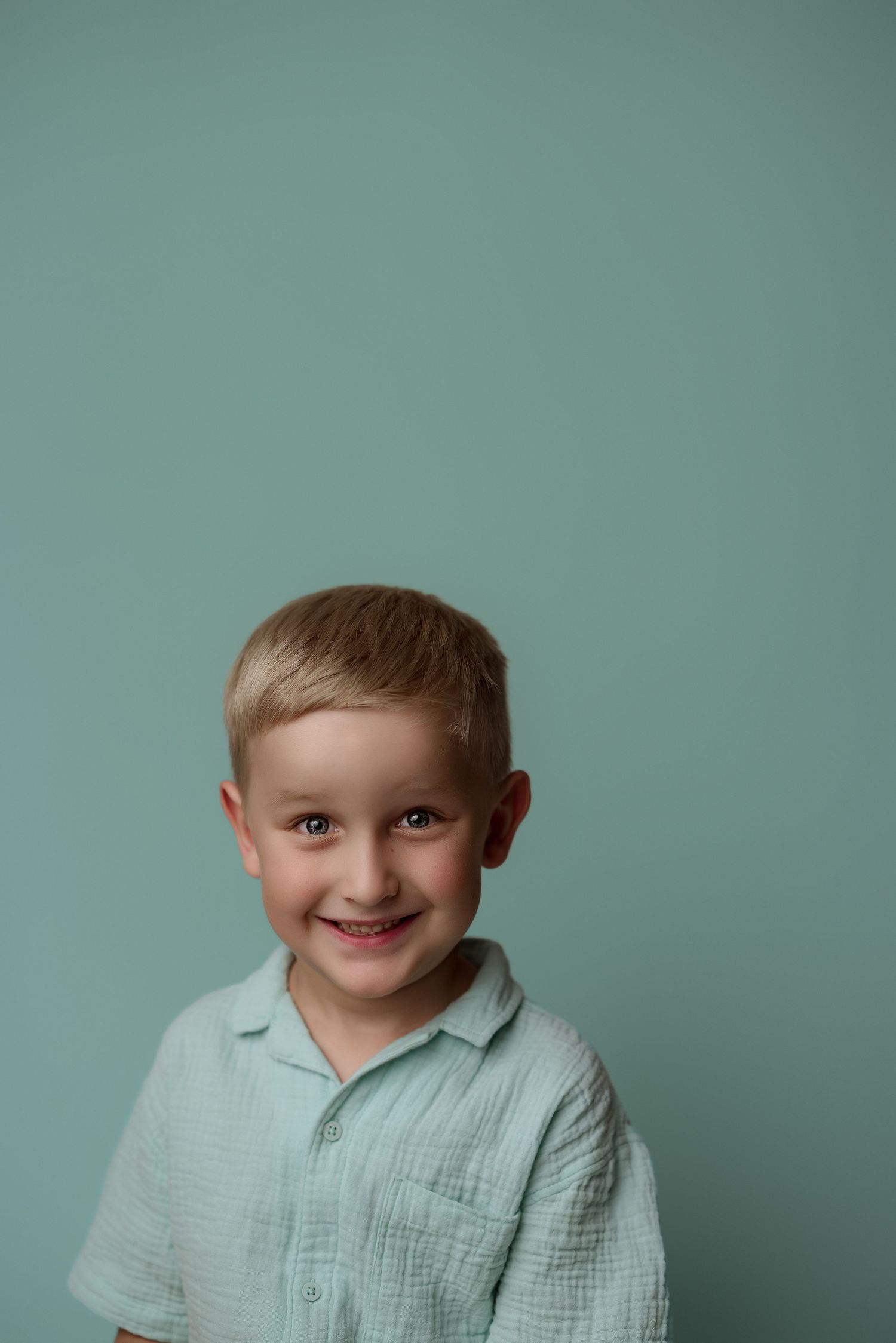 A young child in a mint green shirt smiles warmly against a teal background.