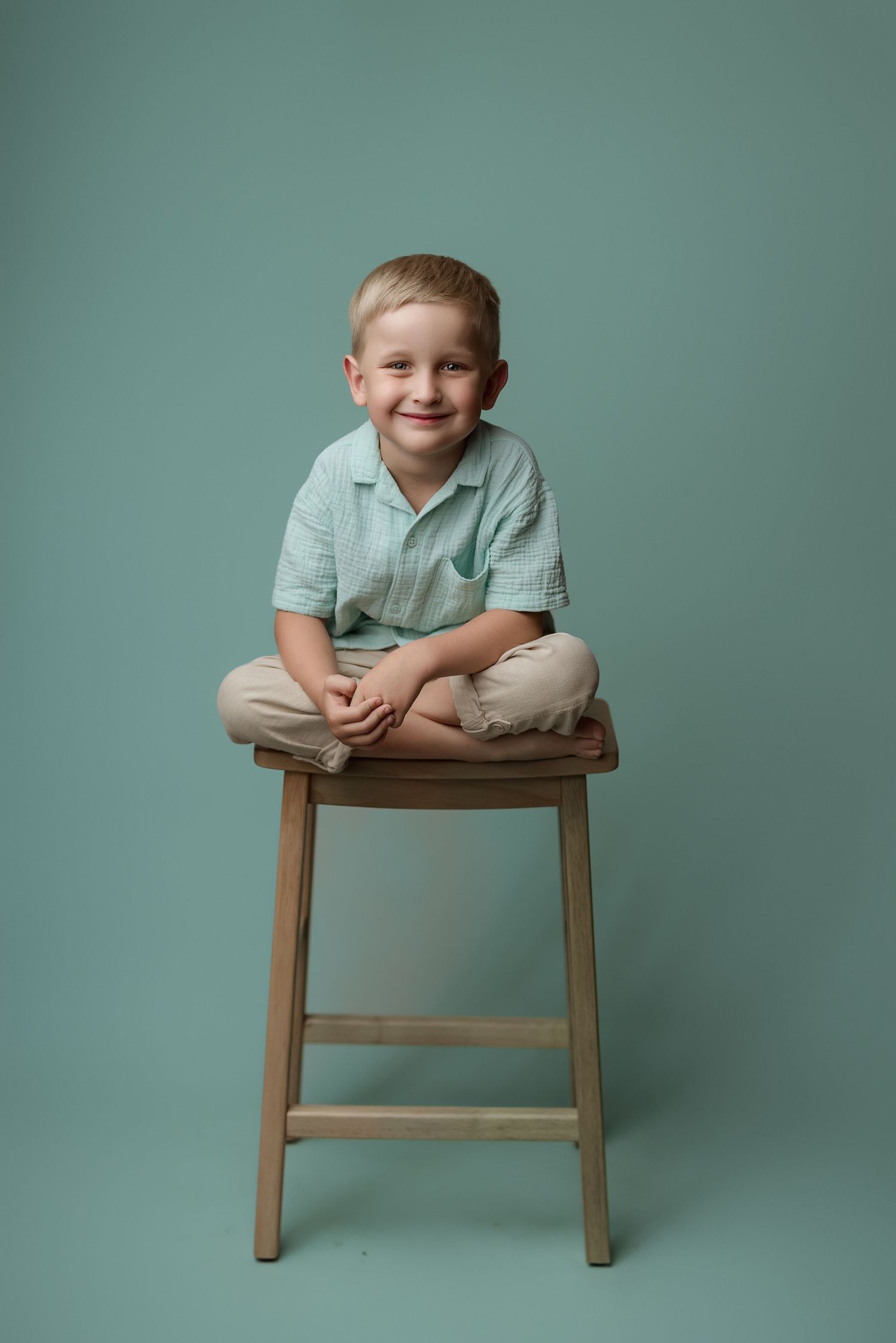 A series of four photos showing a child in a mint green shirt posing playfully on a wooden stool against a teal backdrop.