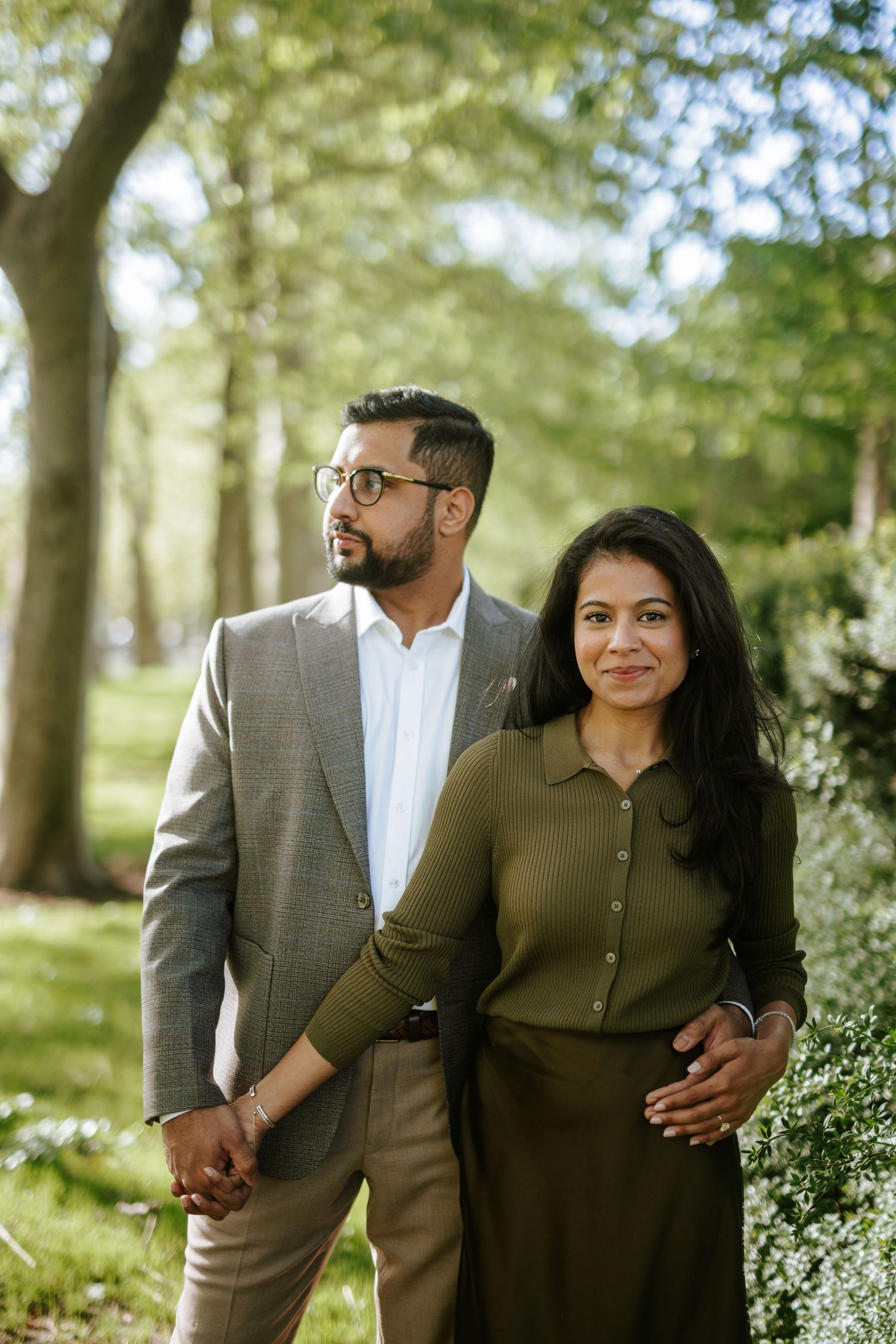 Romantic South Asian engagement photo in a sunlit forest setting, featuring a stylish couple in natural light and elegant attire.