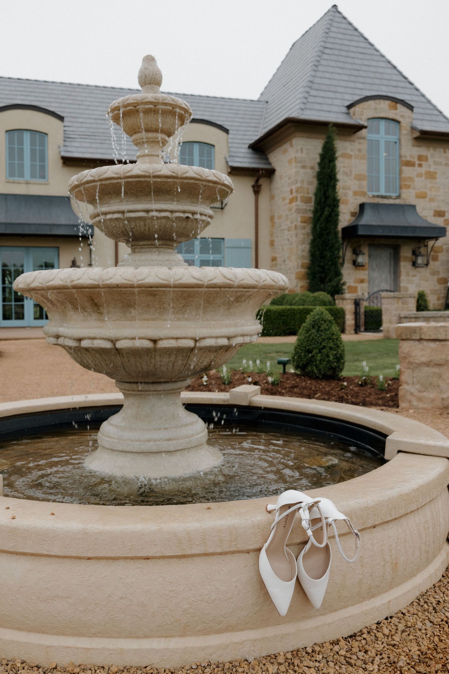 Exterior of The Bower in Edmond Oklahoma with European estate-style architecture with brides shoes displayed on elegant front fountain.
