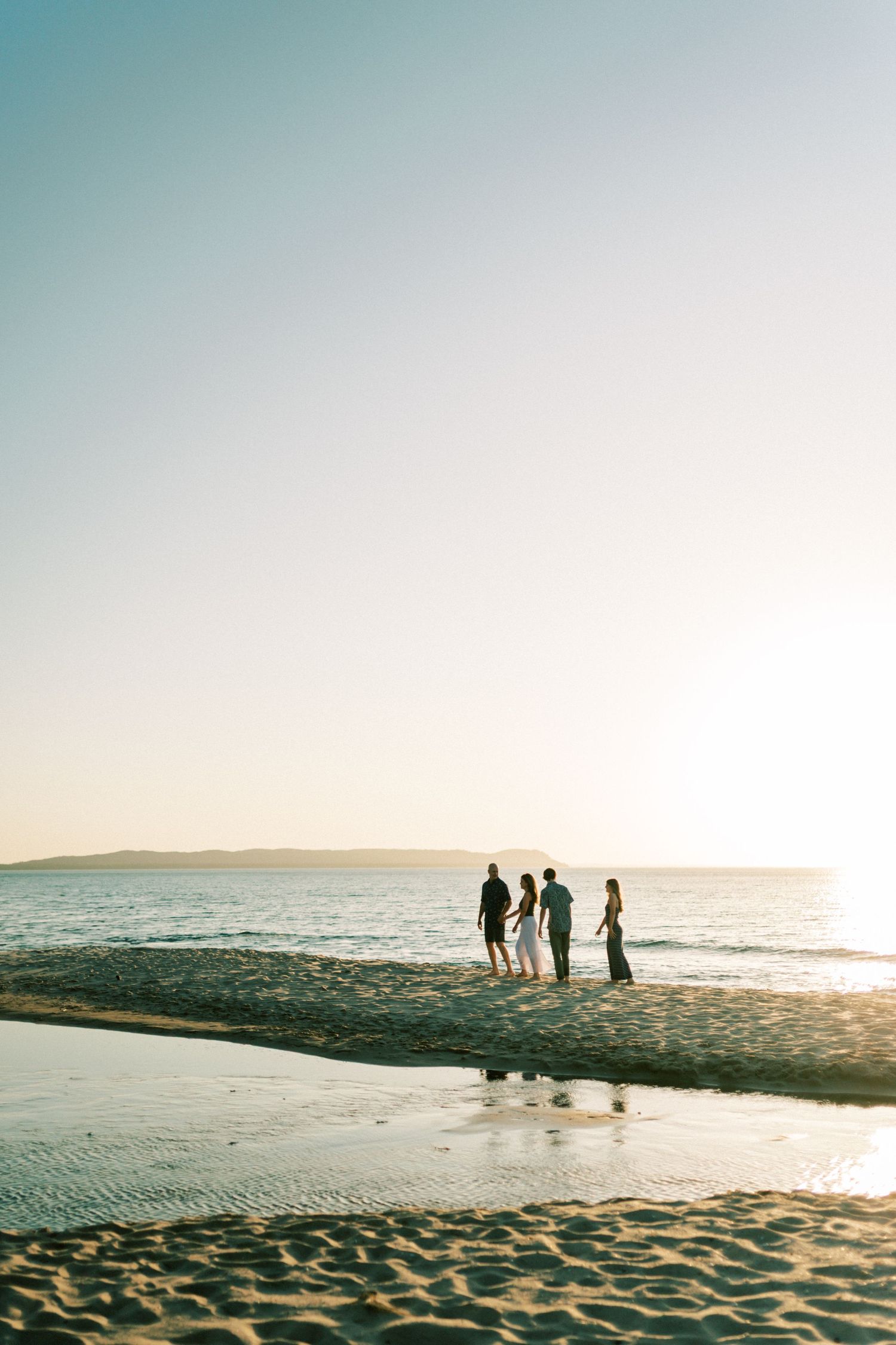 Silhouetted figures walk along a sandy beach at sunset creating shadows on the shoreline.