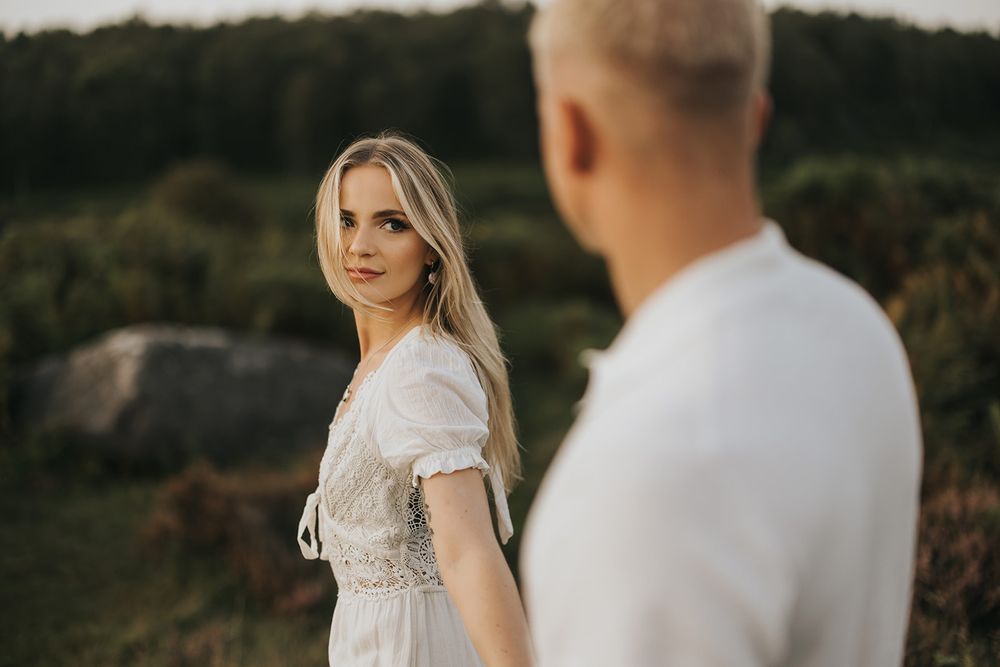 A couple stands on a hilltop during a romantic outdoor photoshoot at golden hour.