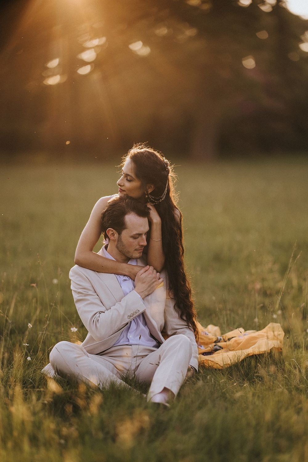 A couple embraces on a grassy field during golden hour as sunlight creates a warm romantic atmosphere.
