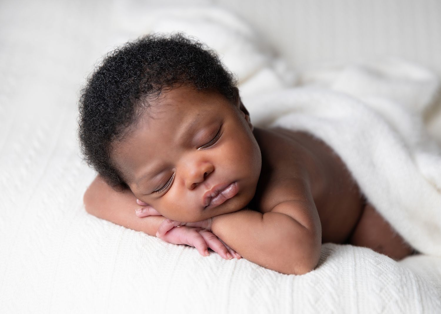 A newborn baby sleeps peacefully on soft white fabric while being photographed from various angles by best newborn photographer in London