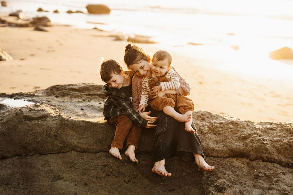A warm sunset scene on a beach with three people sitting together on coastal rocks.