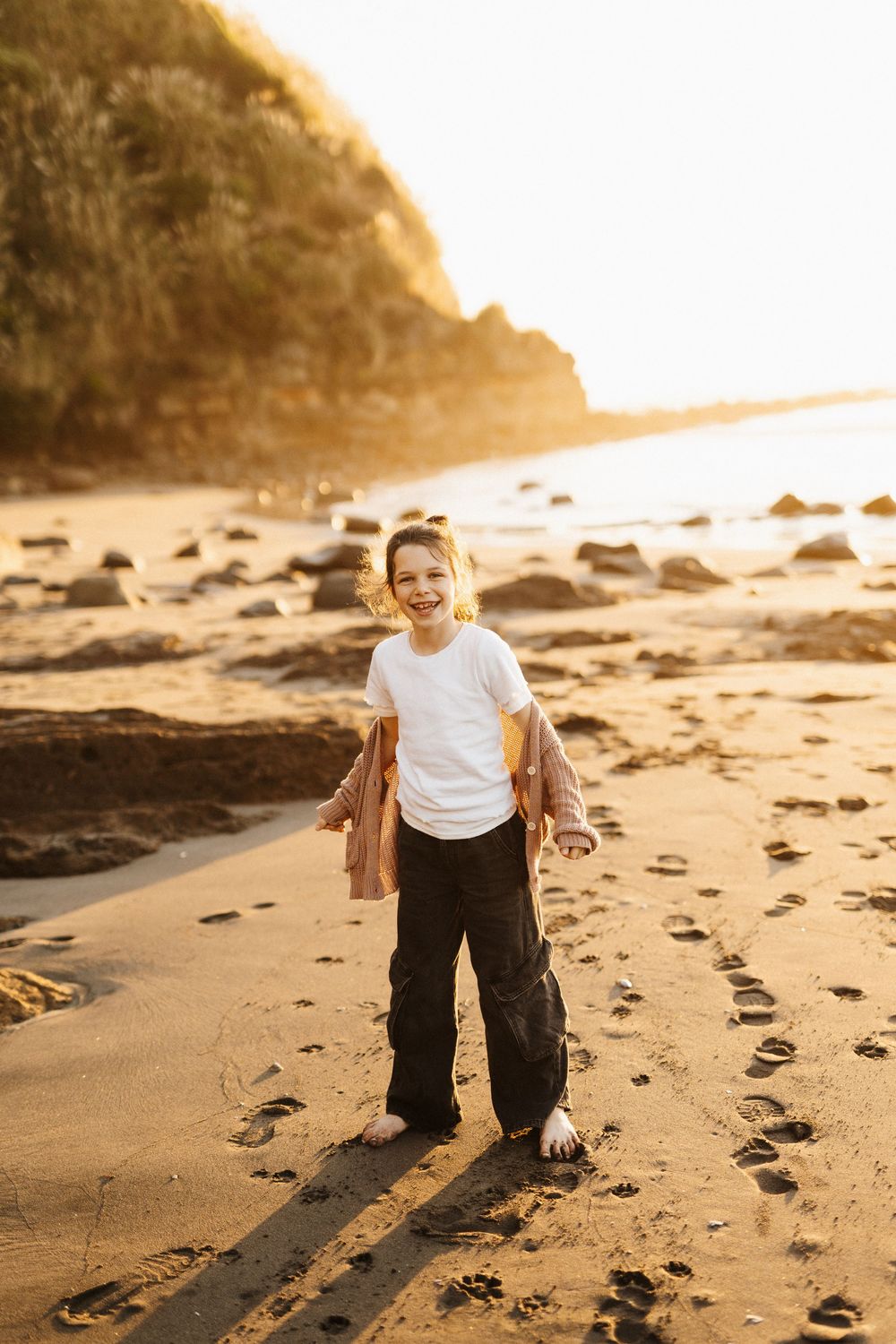 Child in a white t-shirt playing on a rocky beach at sunset.