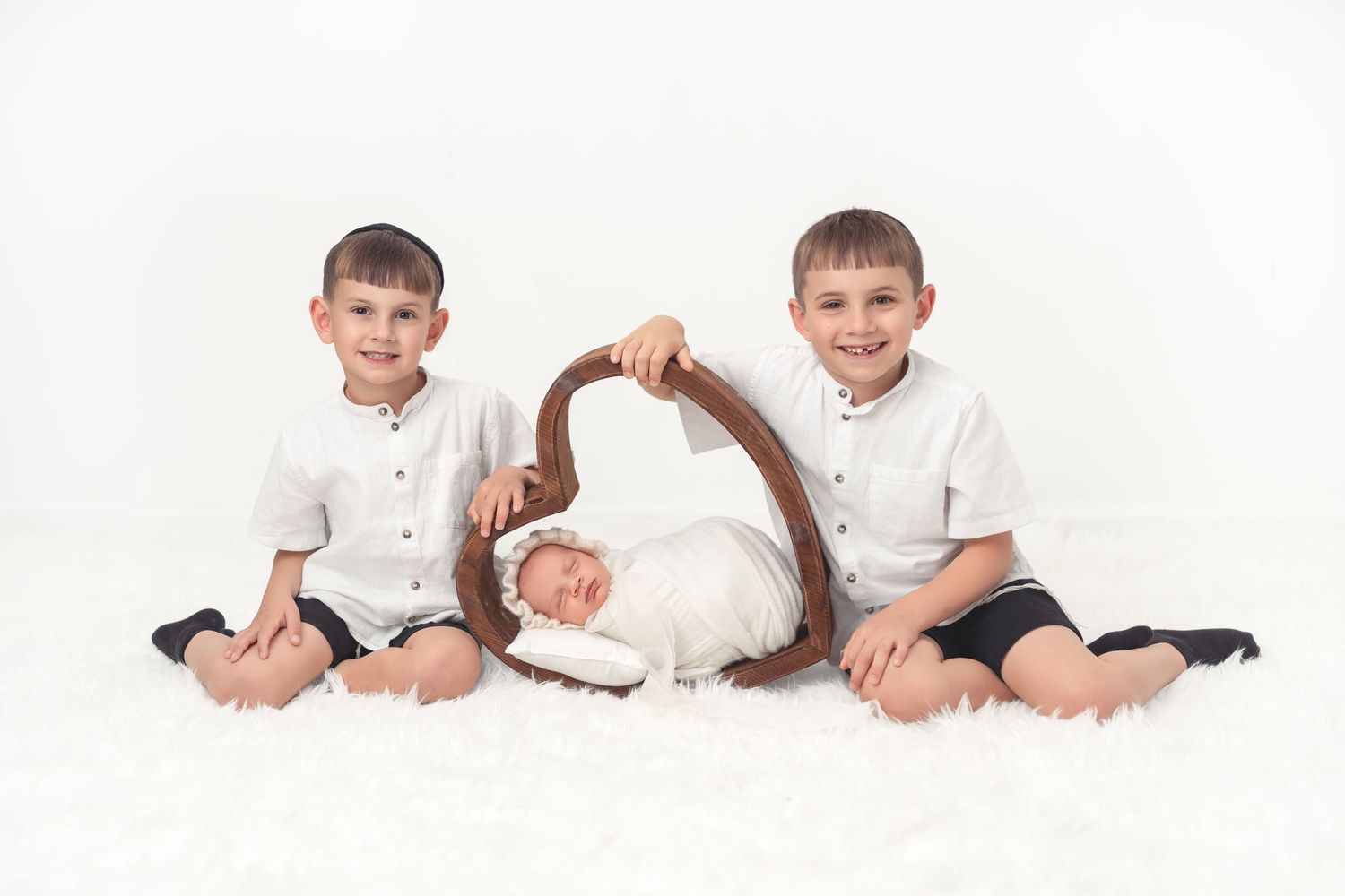 Two young children in white shirts sit on opposite sides of a brown woven basket on a white carpet background.