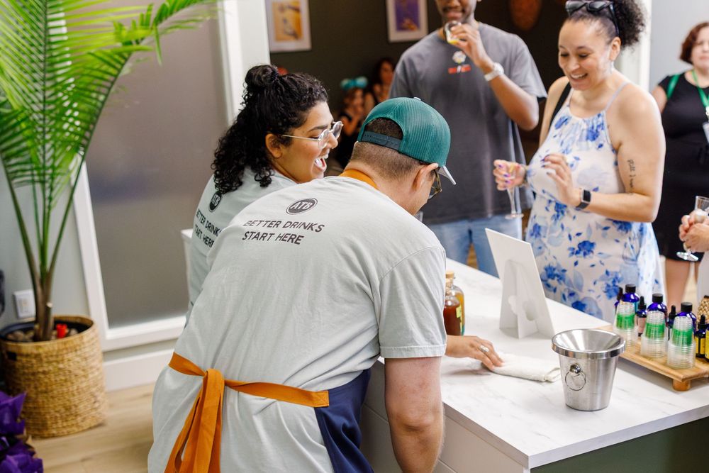 Service staff prepare drinks at a bar counter while customers wait during a social gathering event.