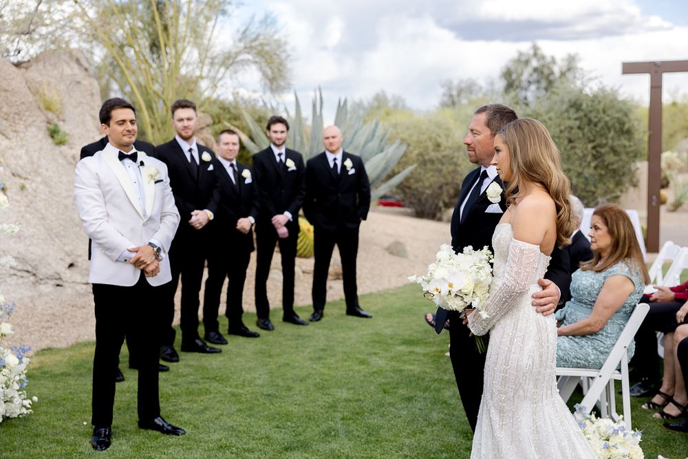 Wedding party members line up along a grassy outdoor venue for candid group photo opportunities at a scenic ceremony.