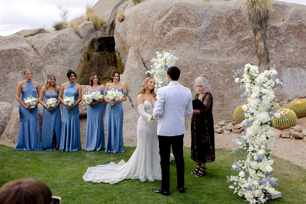 Wedding party stands in front of desert rock formations for outdoor ceremony with white floral arrangements and blue decor.