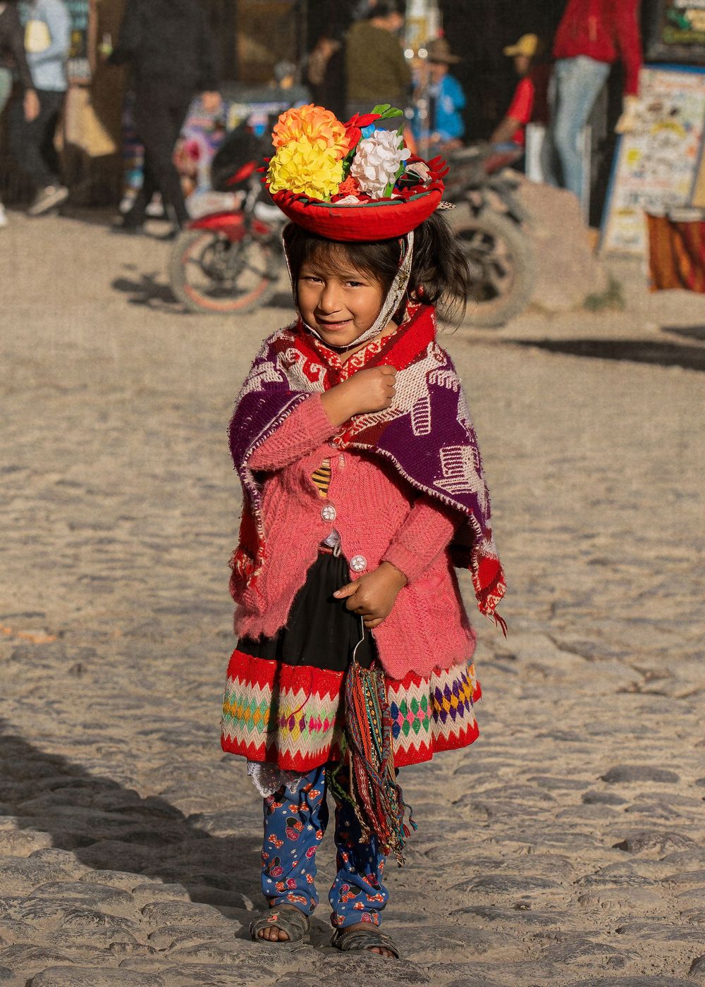 Traditional Peruvian dress with colorful woven patterns and a decorative red hat displayed on a cobblestone street.