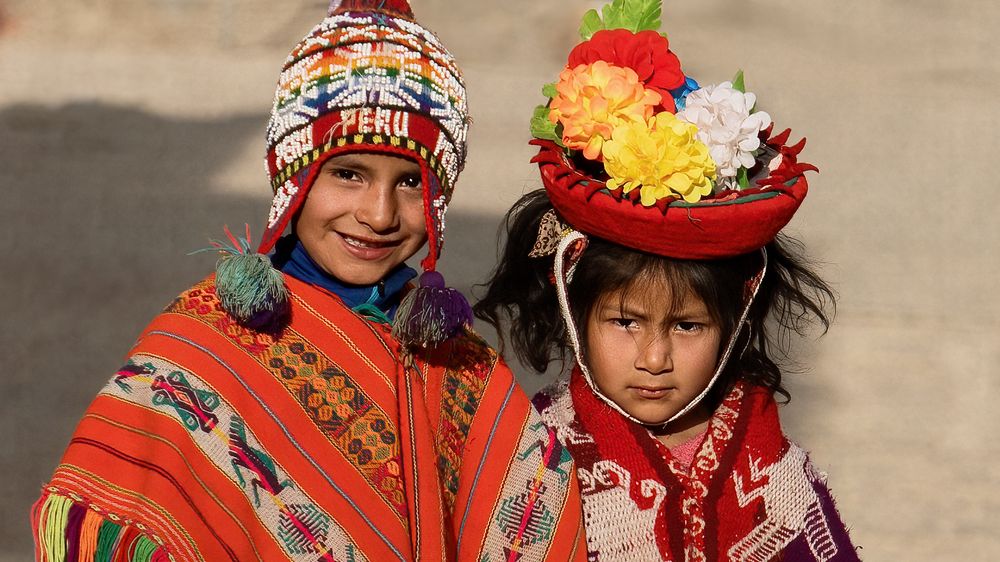 Indigenous artisans in traditional red garments display handmade textiles and crafts at a cultural market in Peru.