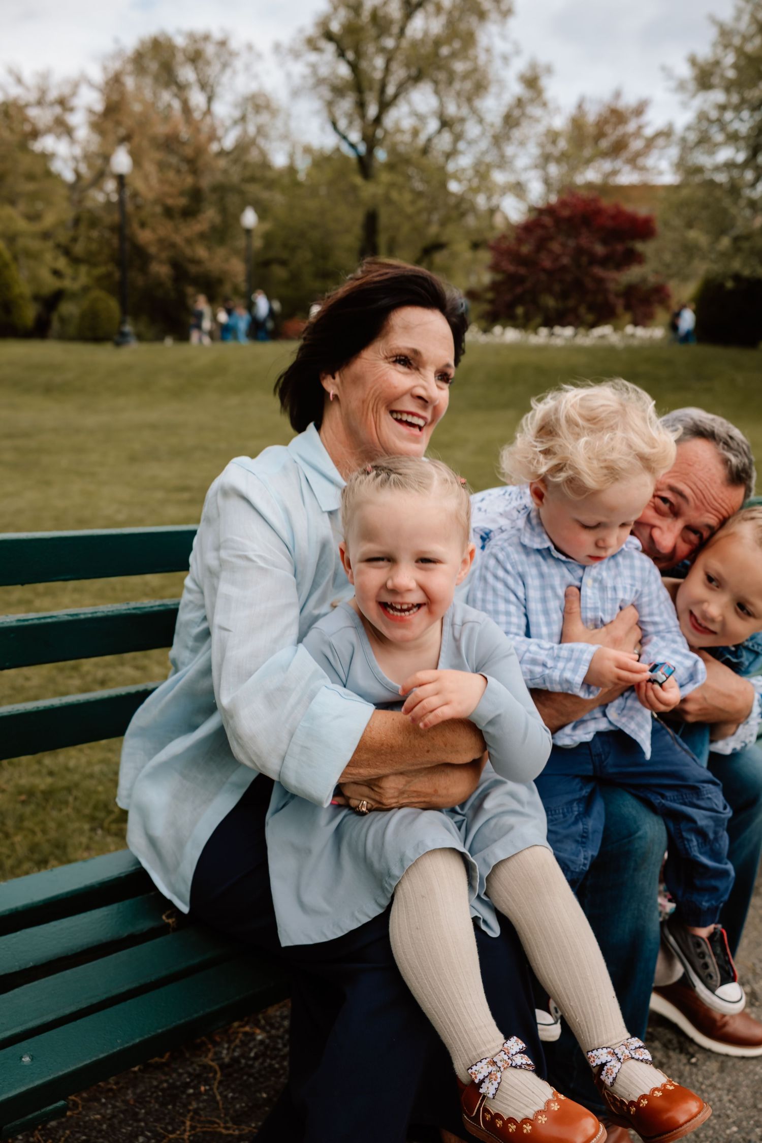 A candid outdoor family moment on a green park bench, filled with joyful laughter on an autumn day.