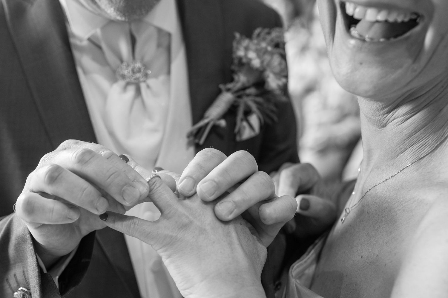 Black and white close-up photo of hands exchanging rings during wedding ceremony.
