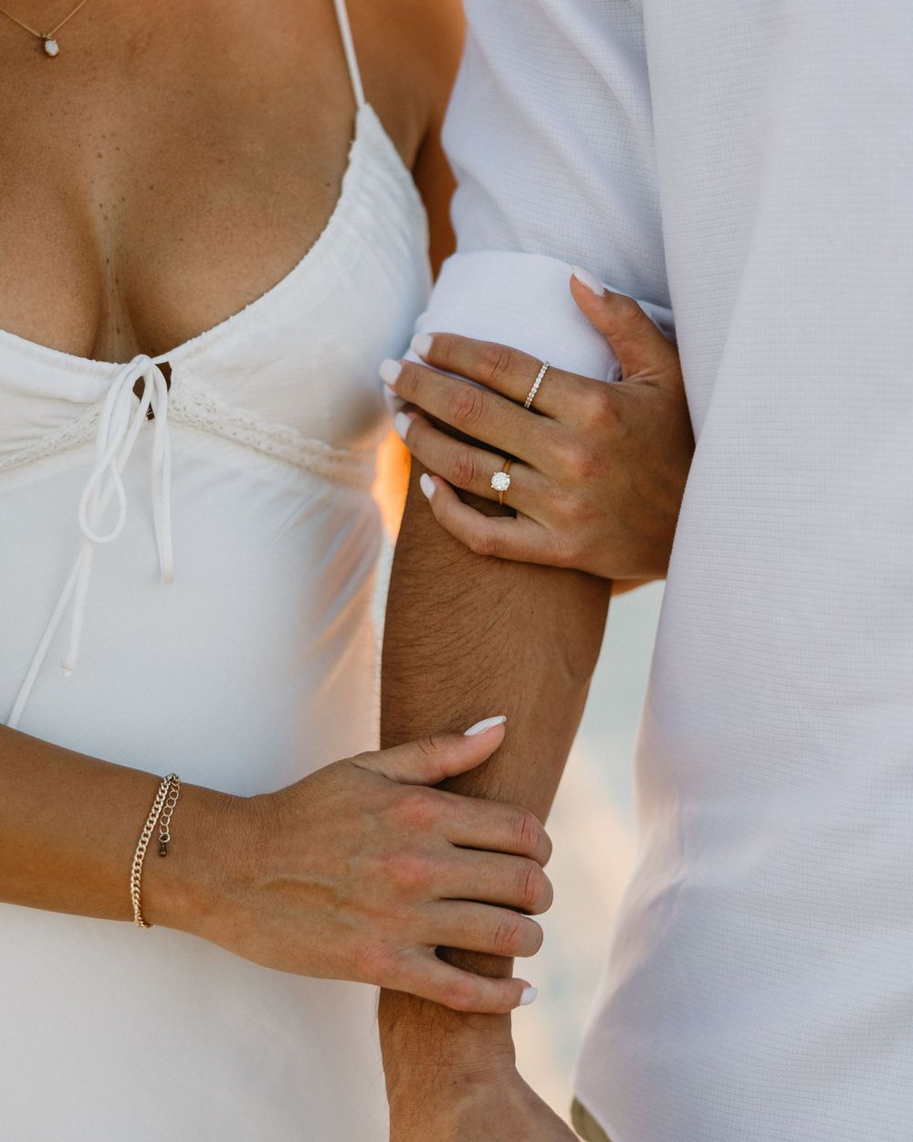 Close-up shot of hands and arms embracing, showing jewelry and white attire details.