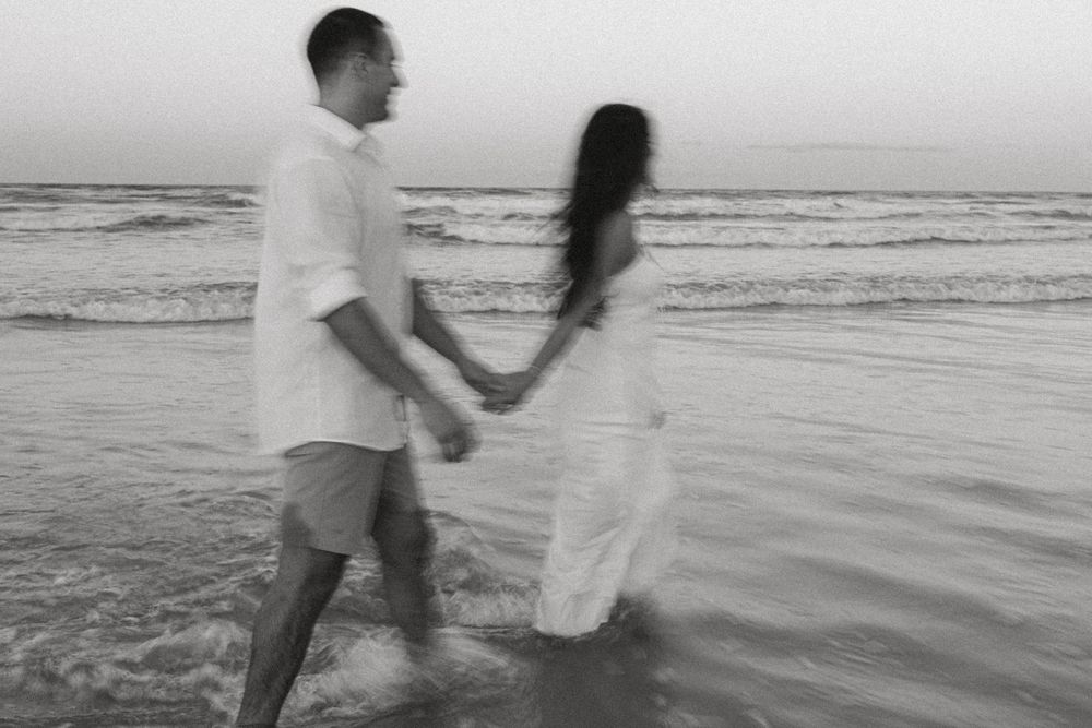 Black and white photo of a couple walking hand in hand in ocean waves.