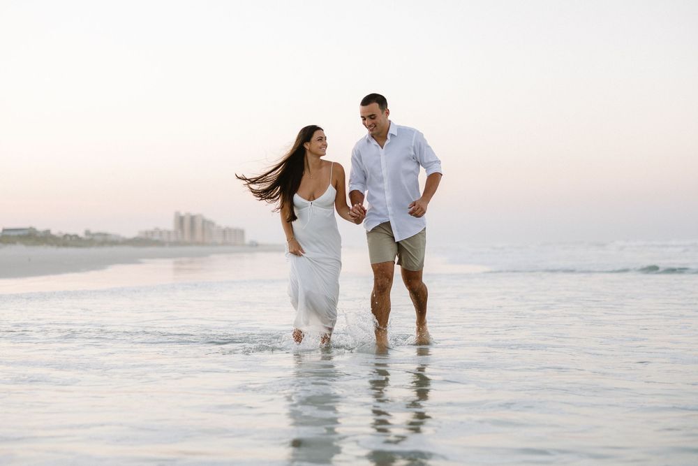 Joyful couple splashing and playing in shallow ocean water at sunset.