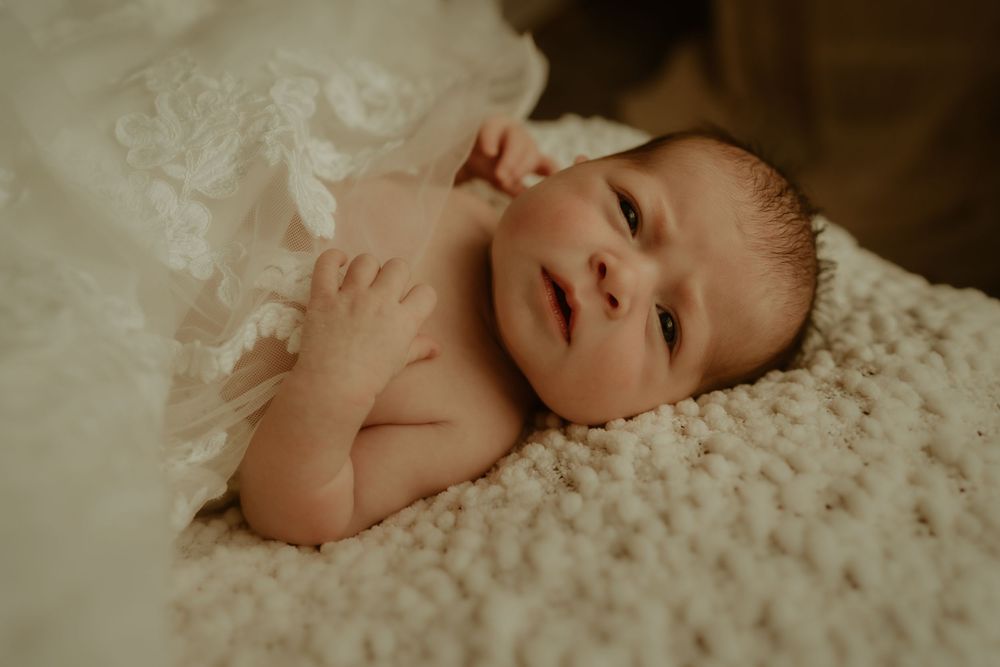 A newborn baby lying on a textured white blanket in warm moody lighting.