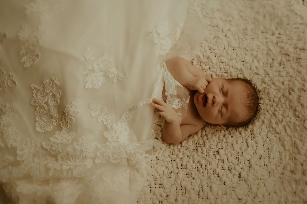 Baby lies peacefully on textured cream-colored blanket in warm, soft lighting.